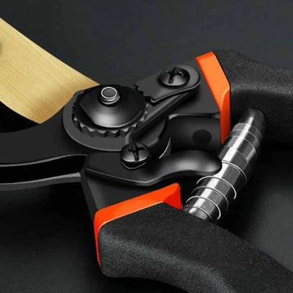 A detailed close-up of the bypass pruning shears' hinge and spring mechanism. The black handle is accented with orange around the joint, and a coiled metal spring provides tension. The central pivot point features a textured knob for adjusting the blade tension.